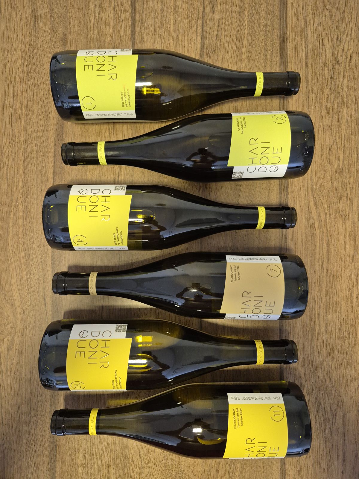 Seis garrafas de Chardonique deitadas lado a lado sobre uma mesa de madeira