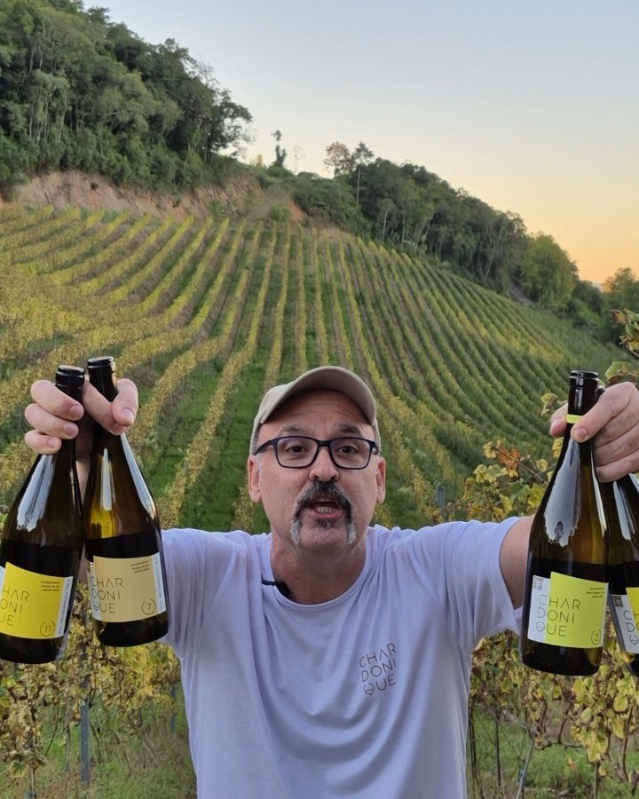 Alexandre Estolano em um vinhedo, segurando garrafas de Chardonique em cada mão